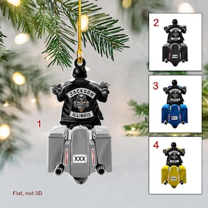 Op de afbeelding: Een plat, niet-3D kerstversiering met een motorrijder op een motorfiets. De versiering is grijs met zwarte accenten en de tekst "Jackson Illinois" en "XXX" op de achterkant. De motorrijder draagt een zwart leren jack met een schedel en kruisbeenderen ontwerp. De versiering is verkrijgbaar in vier verschillende kleuren: zwart, blauw, geel en grijs.