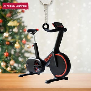 Könnte beinhalten: Ein schwarzer und roter stationärer Heimtrainer-Ornament mit dem Wort "Name" an der Seite. Das Ornament hängt an einer silbernen Kette und einem Ring. Der Text "2D Acrylic Ornament" befindet sich in einem roten Banner oben.