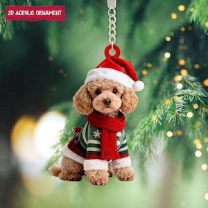 Könnte beinhalten: Ein 2D-Weihnachtsschmuck aus Acryl, der einen Pudel mit Weihnachtsmütze, rotem Schal und grün-rotem Pullover zeigt. Der Anhänger hängt an einer silbernen Kette und trägt den Text "2D Acrylic Ornament".