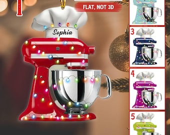 May include: A flat, two-dimensional ornament shaped like a stand mixer with a chef hat, decorated with colorful Christmas lights. The mixer features the name Sophia and is available in red, light blue, dark blue, pink, and lime green colors.