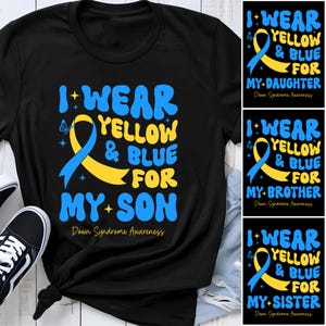 Op de afbeelding: Een zwart t-shirt met een geel en blauw bewustzijnslintje en de tekst I WEAR YELLOW & BLUE FOR MY SON en Down Syndrome Awareness. Het ontwerp bevat kleine ster- en vlinderaccenten in een vetgedrukt, afgerond blauw lettertype.
