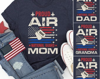 Könnte beinhalten: Marineblaues T-Shirt mit einem verblassten Grafikdesign mit dem Text "PROUD AIR NATIONAL GUARD MOM" über einem amerikanischen Flaggen-Design. Enthält eine Erkennungsmarke mit dem Wort "NAME". Zusätzliche Designs für Papa, Oma und Opa.