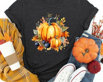 May include: A dark gray t-shirt with a watercolor design of pumpkins, leaves, and berries. The pumpkins are orange and the leaves are red, orange, and yellow.