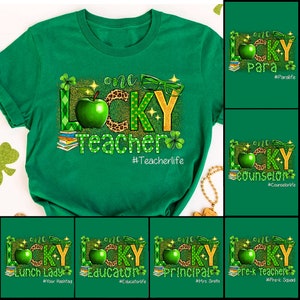 May include: Green t-shirt with a gold and green graphic that says "one lucky teacher" with a green apple, shamrocks, and glasses. The hashtag #Teacherlife is below the graphic.