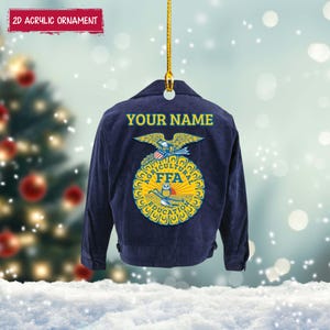 May include: A navy blue acrylic ornament shaped like a jacket. The back of the jacket features the text "YOUR NAME" in yellow, above an FFA emblem. The ornament is suspended by a gold string. The text "2D ACRYLIC ORNAMENT" is in a red banner.