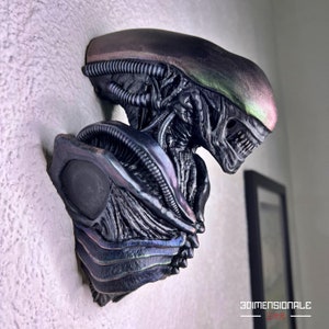 Puede incluir: Un busto de alienígena de escultura negra e iridiscente con una cabeza y un cuerpo detallados. La escultura está montada en una pared.