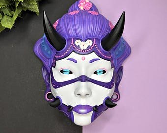 May include: A purple and white demon mask with horns, floral details, and blue accents. The mask has a white face with blue eyes and a purple mouth.