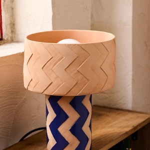May include: A terracotta table lamp with a blue and terracotta chevron pattern. The lampshade is terracotta with a chevron pattern.