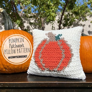 May include: A white crochet cushion with a patchwork pumpkin design in orange, brown, and green. The cushion is sitting on a wooden surface with two real pumpkins on either side. The text "Pumpkin Patchwork Pillow Pattern @Lennyscrochet" is on the pumpkin on the left.
