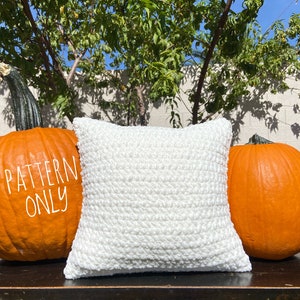 K&ouml;nnte beinhalten: Ein wei&szlig;es geh&auml;keltes Kissen auf einer Holzoberfl&auml;che mit zwei orangefarbenen K&uuml;rbissen auf beiden Seiten. Der Text "PATTERN ONLY" ist auf den K&uuml;rbis links geschrieben.