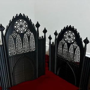 May include: Two black, gothic-style, decorative room dividers with arched tops and intricate window designs. The dividers are made of metal and have a black finish.