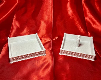 May include: Two white square boxes with decorative edges. One box has a small white post in the centre.