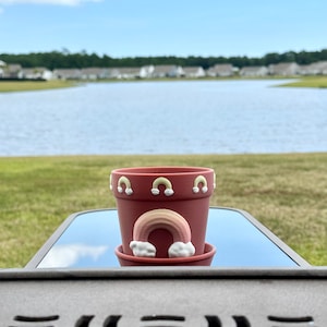 May include: A small terracotta planter with a rainbow and clouds design. The planter is decorated with small yellow and white arches around the rim.