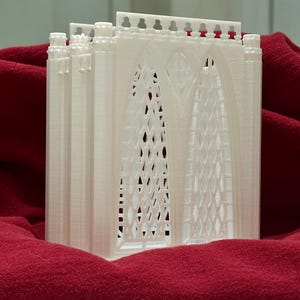 May include: White 3D printed model of a gothic archway with intricate details. The model is made of a smooth, white plastic and has a textured surface.