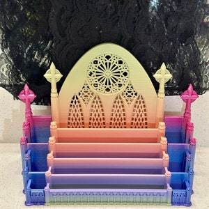 Könnte beinhalten: Ein 3D-gedruckter Schreibtisch-Organizer in Form einer gotischen Kathedrale mit einem Buntglasfenster. Der Organizer ist aus Kunststoff und hat einen Farbverlauf von Pink, Lila und Blau.