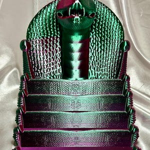 May include: A green and purple 3D printed cobra snake head with a tiered stand. The stand has five levels and is designed to hold items like business cards or small trinkets.