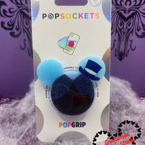 May include: A PopSockets PopGrip featuring a dark blue glittery base and two light blue glittery tops. One top has a top hat design. The PopSockets packaging is white with the PopSockets logo and product information.