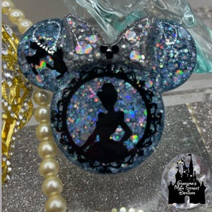 Könnte beinhalten: Ein blaues und silbernes Glitzer-Harz-Mickey-Mouse-Ohrenband mit einer schwarzen Silhouette von Aschenputtel in einem Rahmen. Das Stirnband ist mit einer silbernen Schleife verziert.