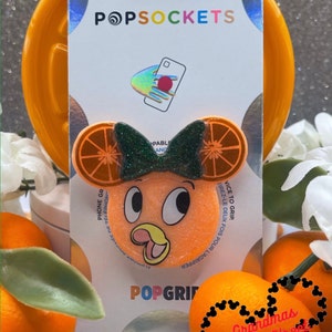 May include: Orange and green phone grip with a cartoon character face and the text "PopGrip" and "Grandmas Main Street Designs".