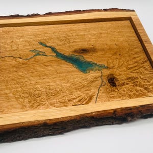 Könnte beinhalten: Ein Holztablett mit einem natürlichen Rindenrand, das einen geschnitzten See mit blauer Harzfüllung zeigt. Das Tablett ist aus hellem Holz mit natürlicher Maserung.