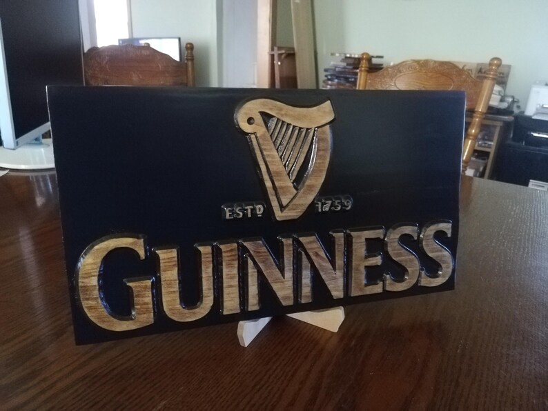 May include: A wooden sign with a black background and a gold Guinness logo. The logo features a harp and the text "ESTD 1759 GUINNESS".