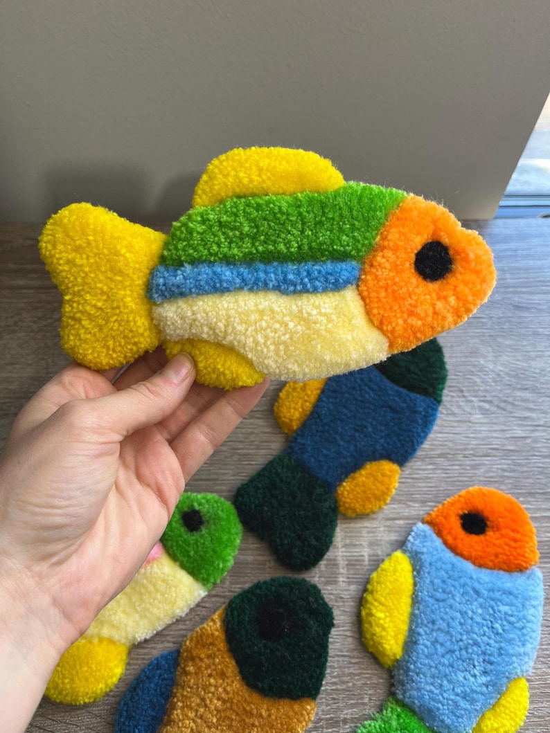 K&ouml;nnte beinhalten: Handgefertigte, fischf&ouml;rmige Dekorationen in verschiedenen Farben. Die Fische sind gelb, gr&uuml;n, blau und orange und bestehen aus einem strukturierten Material. Jeder Fisch hat ein schwarzes Auge. Diese Artikel sind wahrscheinlich f&uuml;r die Inneneinrichtung gedacht.