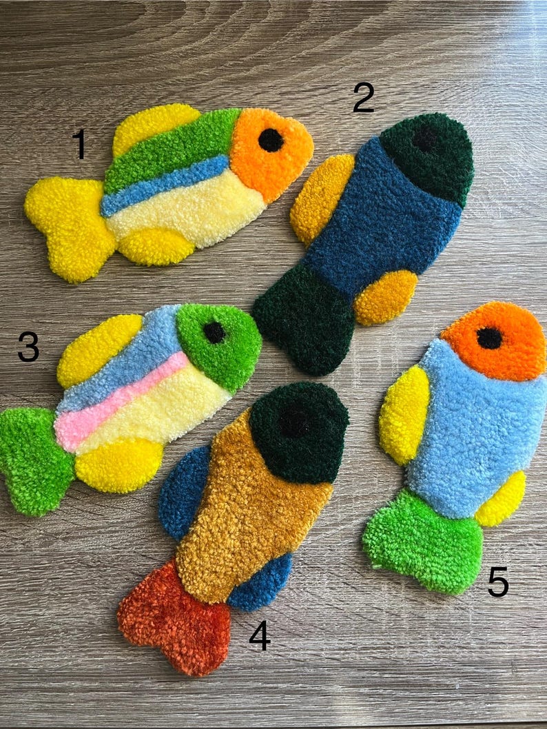 K&ouml;nnte beinhalten: F&uuml;nf handgefertigte, fischf&ouml;rmige Teppiche. Jeder Teppich hat ein einzigartiges Farbschema, darunter Gelb, Gr&uuml;n, Blau, Orange und Rosa. Die Teppiche bestehen aus einem strukturierten, geschlungenen Material und sind wahrscheinlich f&uuml;r dekorative Zwecke bestimmt.