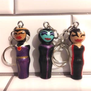 May include: A set of three ceramic mugs with a speckled, cream-colored glaze. Each mug features a different hand-painted floral design in shades of blue, green, and yellow. The mugs have a simple, rounded shape and a comfortable handle.