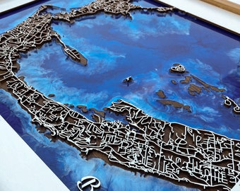 Pode incluir: Um mapa 3D emoldurado das Bermudas com um fundo de resina azul e branco. O mapa é feito de madeira e o contorno da ilha é elevado. A palavra "Bermudas" está escrita em letras brancas na parte inferior da moldura.