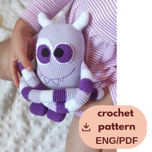 May include: A light purple and white crocheted monster toy with two horns, large white-rimmed eyes with black pupils, and a stitched mouth. The monster has long, striped arms wrapped around its body. Text reads: crochet pattern ENG/PDF.