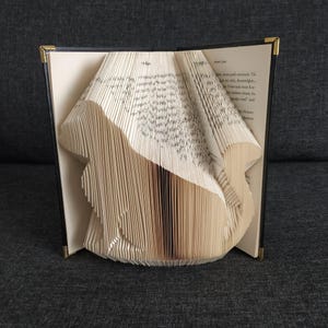 May include: A book with pages folded into the shape of a bird. The book is open and the bird is standing on a table. The book is black with gold accents.