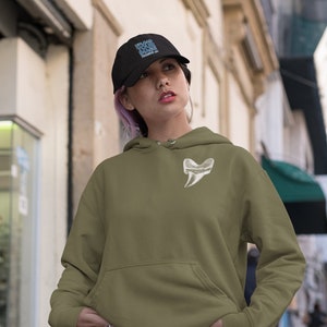 May include: A woman wearing a green hooded sweatshirt with a white tooth graphic on the front. She is wearing a black baseball cap with the text "UPLOAD YOUR LOGO" in blue. She is standing in a city street.