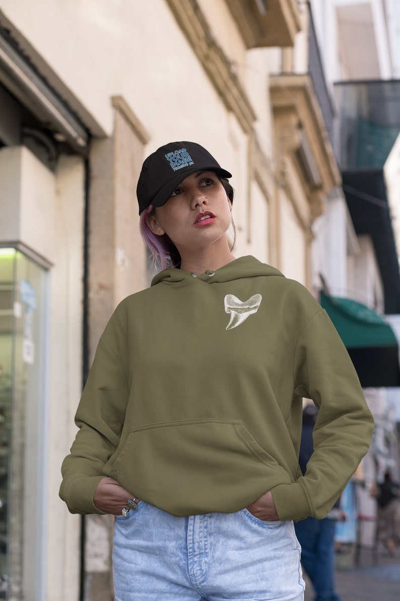 May include: A woman wearing a green hooded sweatshirt with a white tooth graphic on the front. She is wearing a black baseball cap with the text "UPLOAD YOUR LOGO" in blue. She is standing in a city street.