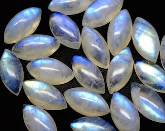 Puede incluir: Una colección de piedras preciosas de piedra lunar de forma ovalada. Las piedras son translúcidas con una base blanca lechosa y exhiben una adularescencia azul. Las piedras preciosas están dispuestas sobre una superficie negra.
