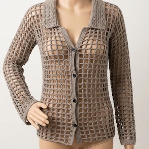 Peut inclure: Cardigan en crochet marron clair à tissage ouvert, avec un col et des manches longues. Le cardigan a une fermeture boutonnée avec trois boutons noirs. Le motif en crochet crée un motif en forme de grille sur tout le vêtement.