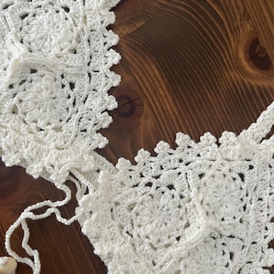 May include: White crocheted bikini top with a delicate floral pattern. The top features adjustable straps and a tie closure at the back.