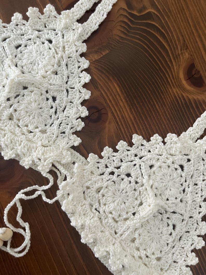 May include: White crocheted bikini top with a delicate floral pattern. The top features adjustable straps and a tie closure at the back.
