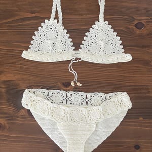 May include: White crochet bikini top and bottom with a delicate floral pattern. The top has adjustable straps and a tie closure at the back. The bottom has a high-waisted fit and a scalloped edge.