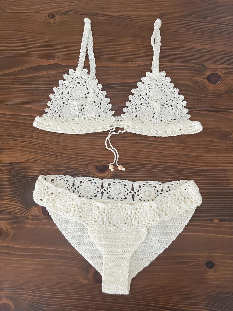May include: White crochet bikini top and bottom with a delicate floral pattern. The top has adjustable straps and a tie closure at the back. The bottom has a high-waisted fit and a scalloped edge.
