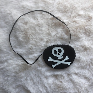 Peut inclure: Un cache-œil noir avec un motif de crâne et d'os croisés blancs. Le cache-œil est attaché à un élastique noir.