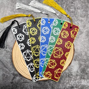 May include: A collection of colorful bookmarks with geometric designs and tassel accents. The bookmarks feature a variety of colors, including black, yellow, blue, green, and red. Each bookmark has a different color tassel, and a geometric design.