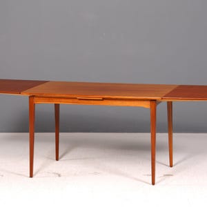 Peut inclure: Une table à manger rectangulaire en bois avec une finition brun chaud, dotée de quatre pieds fuselés et de deux rallonges latérales qui se déploient sous la surface principale pour augmenter la longueur totale du plateau pour plus de places.