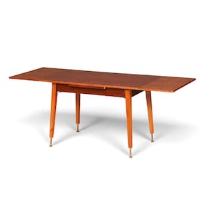 Könnte beinhalten: Ein rechteckiger Holzesstisch mit einer glatten, mittelbraunen Oberfläche. Der Tisch hat vier konisch zulaufende Beine, die jeweils in einer zylindrischen Metallkappe enden. Das Design umfasst ein ausziehbares Element auf der rechten Seite.