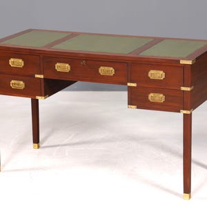 Op de afbeelding: Een mahoniehouten bureau met een groen leren blad en messing hardware. Het bureau heeft zes laden en vier poten met messing accenten. Het bureau is ongeveer 152 cm breed, 76 cm diep en 76 cm hoog.