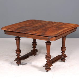 Könnte beinhalten: Ein kleiner, antiker Holztisch mit quadratischer Tischplatte und gedrechselten Beinen. Der Tisch ist aus dunkelbraunem Holz gefertigt und hat eine dekorative Zarge. Der Tisch ist ca. 61 cm lang und breit, und 71 cm hoch.