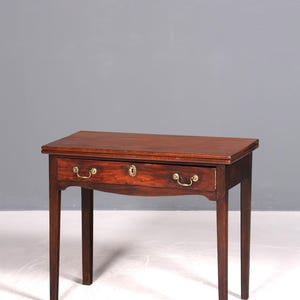 Può includere: Un tavolo in legno marrone scuro con piano rettangolare e due cassetti. I cassetti hanno maniglie in ottone e una serratura. Il tavolo ha quattro gambe sottili. Un mobile classico.