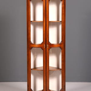 Puede incluir: Una vitrina alta de madera con puertas de cristal. El mueble es de un color marrón cálido y rico y presenta dos puertas de cristal con adornos decorativos. En el interior, hay varios estantes para exhibir objetos. El mueble tiene una base curva y una parte superior detallada.