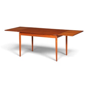 Könnte beinhalten: Ein rechteckiger Esstisch aus Holz mit warmbrauner Oberfläche und glatter Tischplatte. Der Tisch verfügt über vier konisch zulaufende Beine und zwei ausziehbare Seitenplatten, die unter der Hauptplatte hervorgezogen werden können.