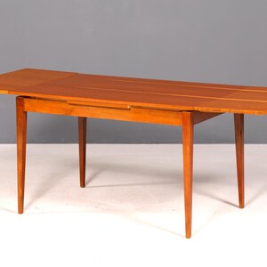 Peut inclure: Table en bois avec une finition brun-rougeâtre chaleureuse. Le dessus rectangulaire est doté d'un système de rallonge et de quatre pieds effilés. La table mesure environ 152 cm de long lorsqu'elle est entièrement déployée.
