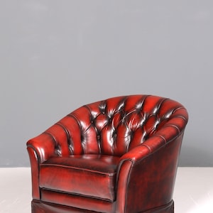 Könnte beinhalten: Ein roter Ledersessel mit getufteter Rückenlehne und Sitzfläche. Der Stuhl hat eine geschwungene Rückenlehne und Armlehnen sowie einen gerockten Sockel. Das Leder hat eine glänzende Oberfläche. Der Stuhl ist ein klassisches Möbelstück.